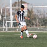A teenage soccer player dribbles the ball on an outdoor football field during the day.